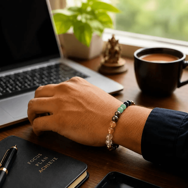 dhan-yog-bracelet-worn-on-wrist-lifestyle Man wearing Dhan Yog crystal bracelet on left wrist at work desk with laptop, journal and coffee